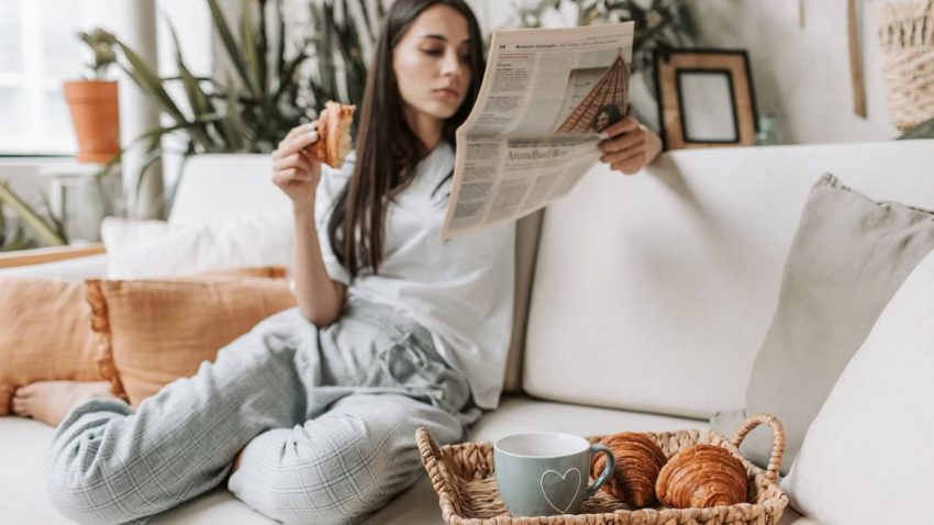 Relaxing morning scene with a woman enjoying coffee and a newspaper on a cozy couch.