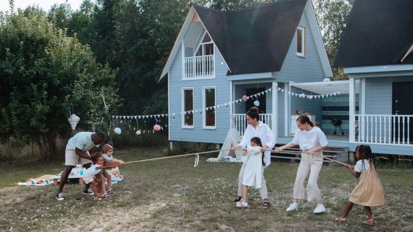 Happy family playing tug of war in front of cozy houses during a summer day.